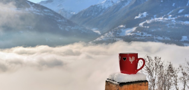 Ver en una taza roja puesta en un poste nevado de una terraza sobre un mar de nubes en la montaña