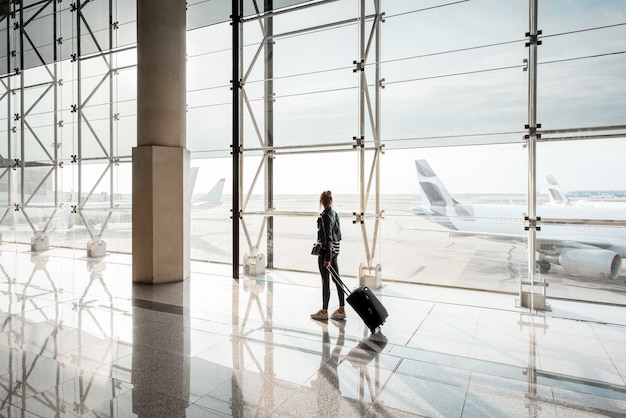 Ver en la ventana del aeropuerto con una mujer caminando con maleta en la sala de salidas del aeropuerto. Vista de gran angular con espacio de copia
