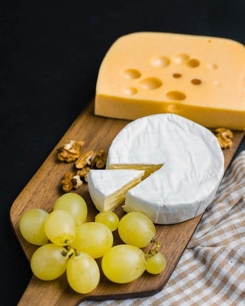 Veränderung des Käses, der Nüsse und der Trauben auf hölzernem Schneidebrett. Camembert und Edamer Käse. Essen für Wein und Romantik, von oben gesehen.