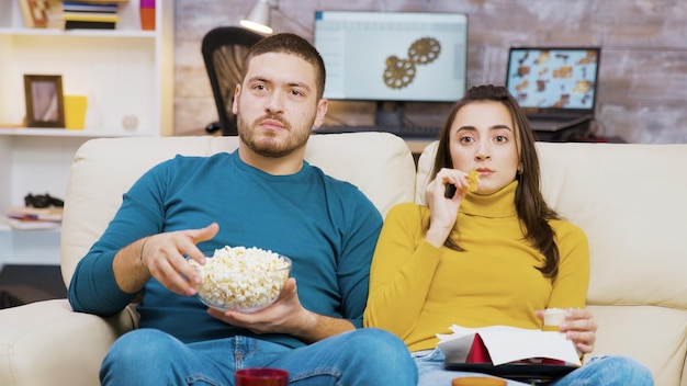 Verängstigte Paare, die fernsehen und Pizza und Popcorn essen, die auf der Couch sitzen. Paare, die Junk-Food essen.