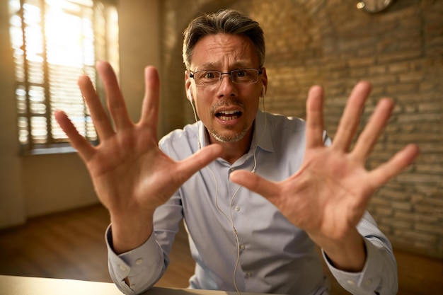 Verängstigter Geschäftsmann, der gestikuliert, hör auf zu singen, während er im Büro arbeitet und in die Kamera schaut