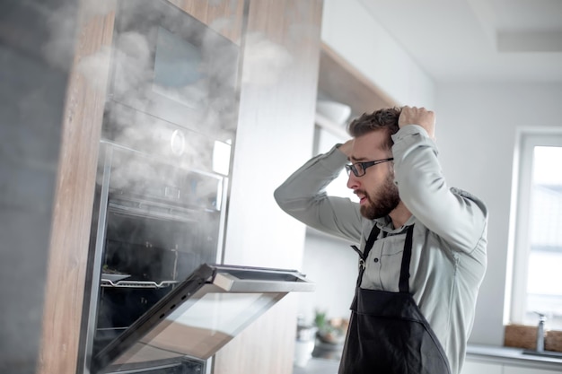 Foto verängstigter mann, der in der nähe eines mit rauch gefüllten ofens steht