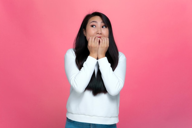 Verängstigtes junges asiatisches Mädchen, das nervös nagende Nägel fühlt, macht erschreckende oder panische Gesten