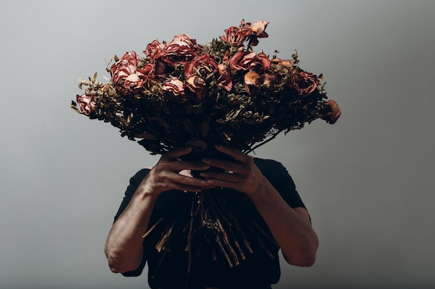 Verärgerte ältere Frau hält verwelkten trockenen alten Rosenblumenstrauß