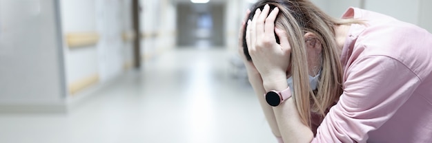Verärgerte Frau in medizinischer Schutzmaske sitzt im Krankenhausflur