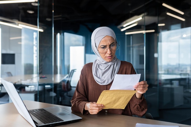 Verärgerte Geschäftsfrau im Hijab, die im Büro arbeitet, erhielt einen Briefumschlag mit schlechter Post