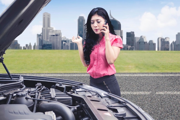 Verärgerte Geschäftsfrau spricht am Telefon und bittet um Hilfe bei der Reparatur eines kaputten Autos