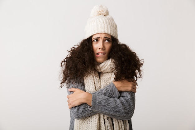 Foto verärgerte junge frau, die winterschal trägt, der lokal über weißer wand steht und zittert