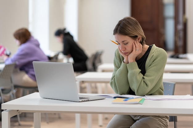 Verärgerte reife Studentin, die an schwierigen Hausaufgaben in der Bibliothek arbeitet, müde vom Lernen