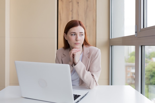 verärgerte rothaarige Geschäftsfrau, die am Computer arbeitet und im Büro sitzt