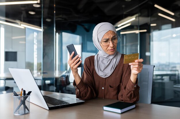 Verärgerte und enttäuschte Frau im Hijab im Büro, die versucht, im Online-Shop einzukaufen