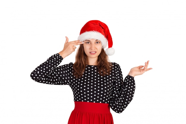 Verärgerte und missfallene Frau im Kleid, das Finger auf Tempel zuckt und hält. emotionales Mädchen im Weihnachtsmann-Weihnachtshut getrennt auf Weiß. Urlaub