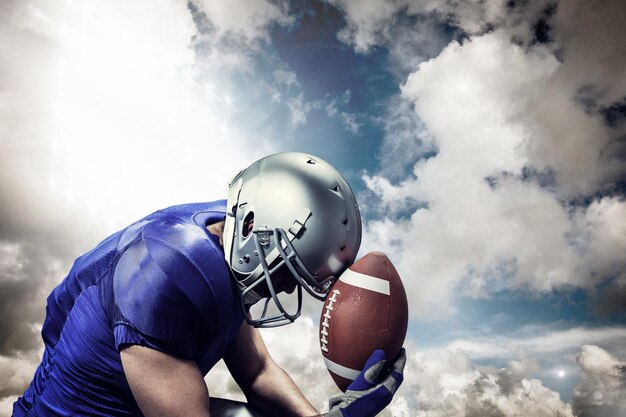 Verärgerter American-Football-Spieler mit Ball gegen Scheinwerfer im Himmel