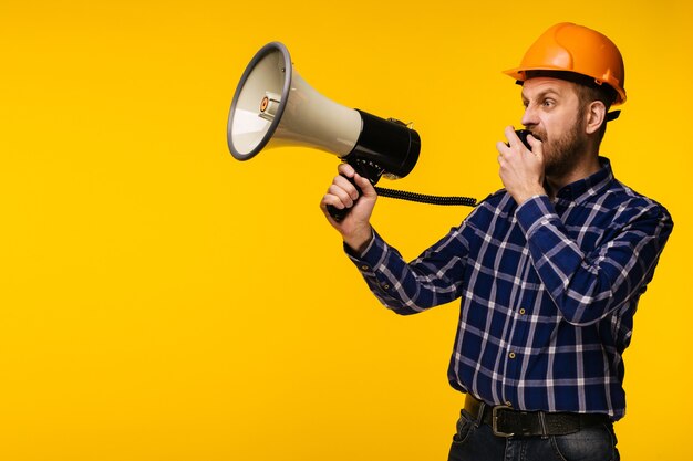 Verärgerter Arbeitermann im orangefarbenen Helm mit einem Megaphon auf gelbem Hintergrund - Bild