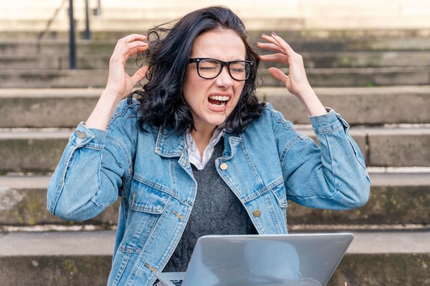 Verärgerter Frauenschulungskurs, der in der Stadt arbeitet und Online-Bildungswebinar mit Laptop anschaut