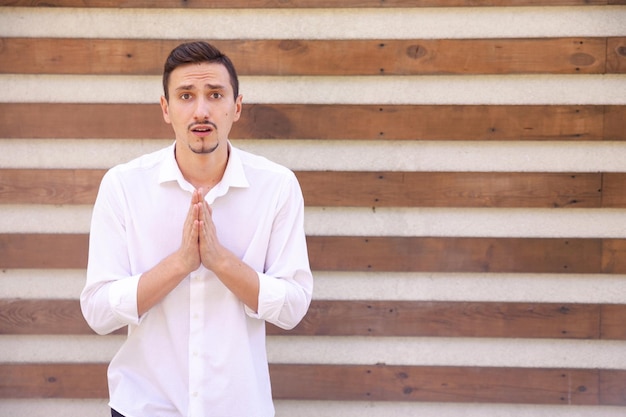 Verärgerter kaukasischer bärtiger Kerl, der um Hilfe bittet und mit gefalteten Handflächen zu Gott betet