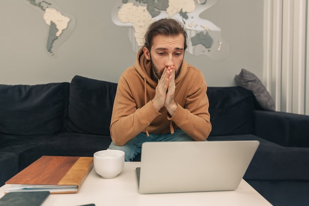 Verärgerter Mann schaut auf Laptop, während er auf dem Sofa sitzt