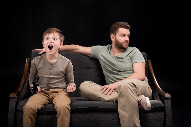 Verärgerter Vater sitzt auf dem Sofa in der Nähe des kleinen Sohnes, der mit dem Konzept der Joystick-Familienprobleme spielt