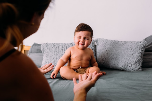 Verärgertes Baby weint auf dem Bett im Zimmer sitzend in Shorts