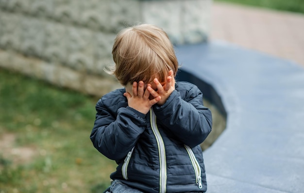 Verärgertes Kind bedeckt zu Hause sein Gesicht. Kind versteckt sich hinter seinen Handflächen