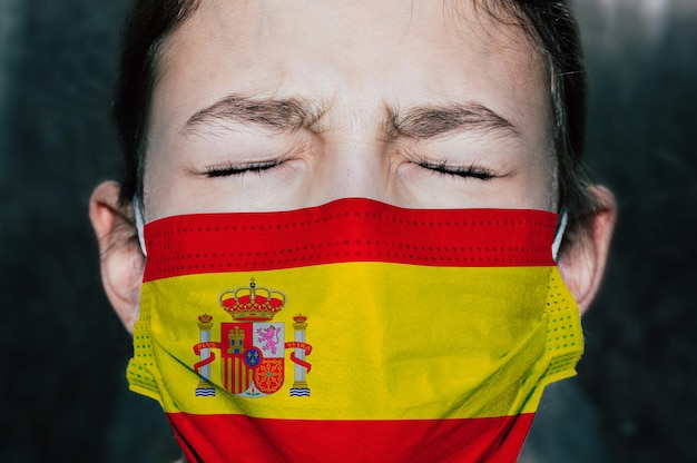 Verärgertes Teenager-Mädchen in medizinischer Maske mit der Flagge Spaniens