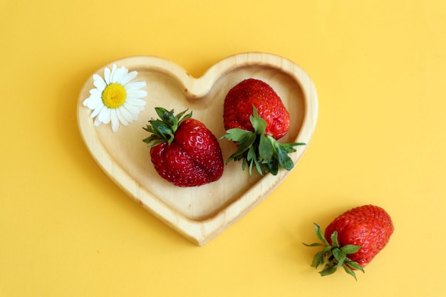 El verano es la época de las bayas de vitamina fresas jugosas en un plato de madera en forma de corazón fondo amarillo vista superior primer plano espacio para texto