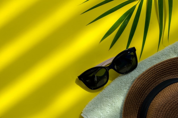 Verano gafas de sol toalla y sombrero sobre fondo amarillo con hojas al lado