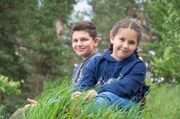 En verano, un hermano y una hermana se sientan en la hierba del bosque.