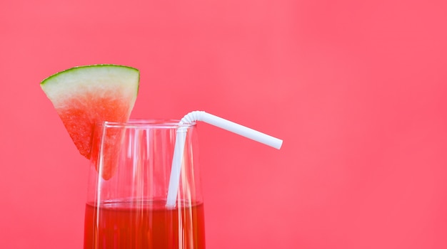 Verano del jugo de la sandía con la fruta de la sandía del pedazo sobre el vidrio en fondo rojo