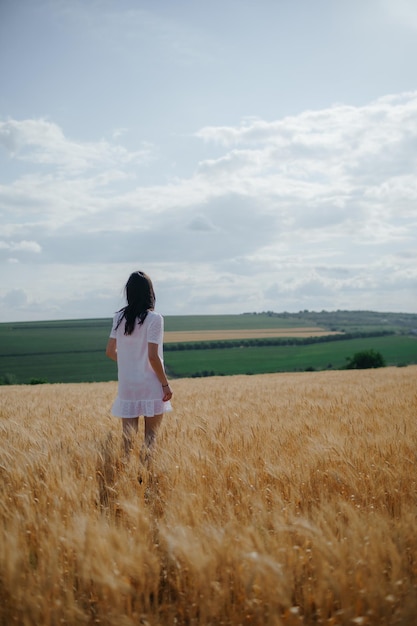 Foto el verano. mujer joven caminando en un campo de trigo dorado