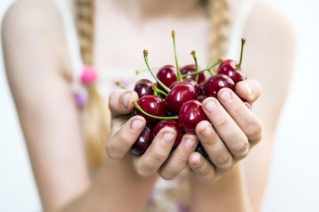 Verano: la niña sostiene una cereza roja madura en sus manos