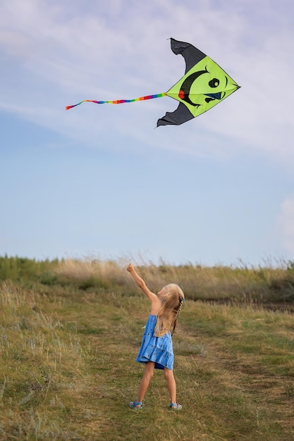 En verano, una niña vuela una cometa en el campo. Juega al aire libre en el parque al atardecer. El niño juega en la naturaleza.