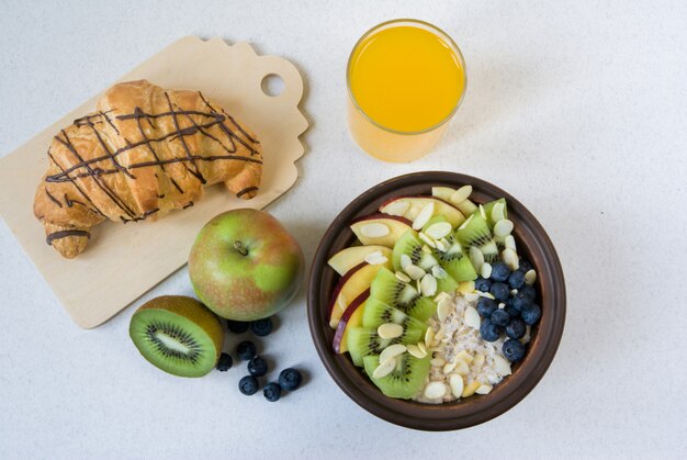 Verano saludable desayuno o merienda. Avena con bayas y frutas, jugo y krassan sobre una mesa plana blanca