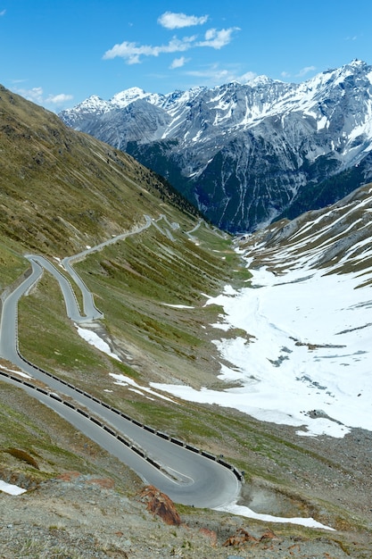 Verano Stelvio Pass con nieve en la ladera de la montaña y carretera serpenteante (Italia)