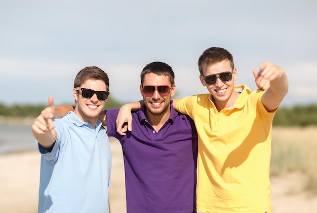 verano, vacaciones, vacaciones, gente feliz concepto - grupo de amigos divirtiéndose en la playa y apuntando a ti