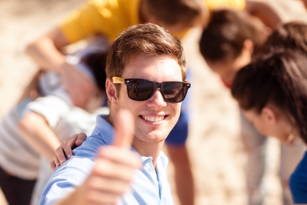 verano, vacaciones, vacaciones, gente feliz concepto - hombre con un grupo de amigos en la playa mostrando los pulgares para arriba