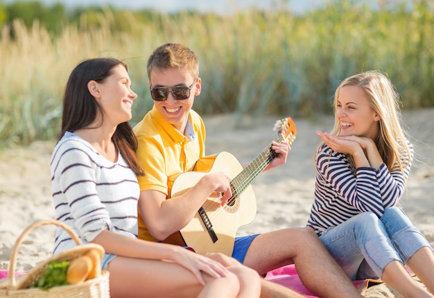 verano, vacaciones, vacaciones, música, gente feliz concepto - grupo de amigos con guitarra divirtiéndose en la playa