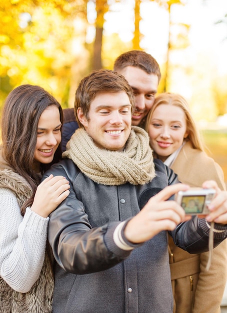 verano, vacaciones, vacaciones, viajes, turismo, concepto de gente feliz: grupo de amigos o parejas que se divierten con una cámara de fotos en el parque de otoño