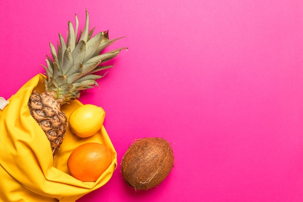 Verão, conceito de férias. Frutas tropicais com um saco de algodão amarelo sobre um fundo rosa