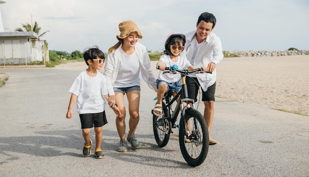 Verão divertido no mar Pais felizes guiam seus filhos a aprender a andar de bicicleta em uma praia de areia Sorridos capacetes de segurança e liberdade de ciclismo caracterizam este conceito alegre de dia de turismo