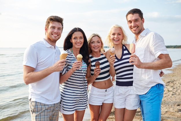 verão, férias, mar, turismo e conceito de pessoas - grupo de amigos sorridentes comendo sorvete na praia