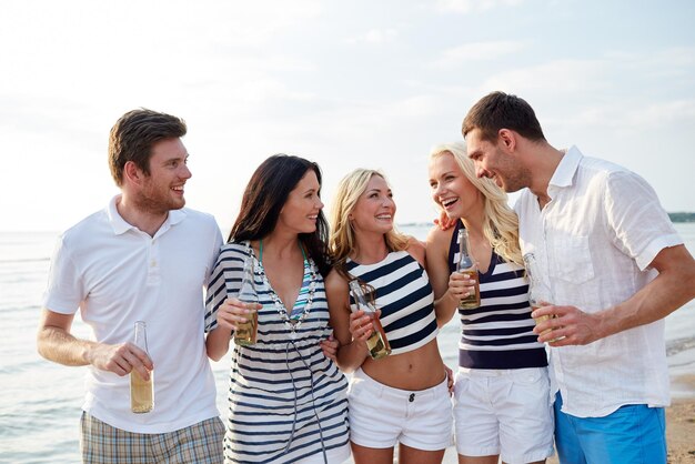 verão, férias, turismo, bebidas e conceito de pessoas - grupo de amigos sorridentes com garrafas bebendo cerveja ou cidra na praia