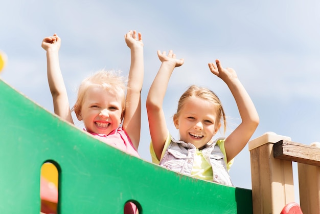 verão, infância, lazer, amizade e conceito de pessoas - meninas felizes acenando as mãos no quadro de escalada do parque infantil