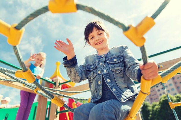 verão, infância, lazer, gesto e conceito de pessoas - menina feliz acenando com a mão no quadro de escalada do parque infantil