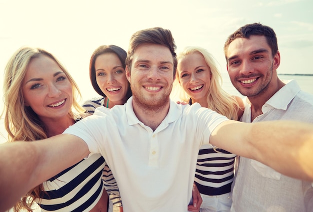 verão, mar, turismo, tecnologia e conceito de pessoas - grupo de amigos sorridentes com câmera na praia fotografando e tirando selfie