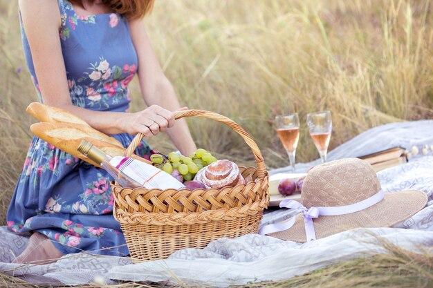 Verão - piquenique no prado. garota segurando uma cesta para um piquenique com baguete, vinho, taças, uvas e pãezinhos