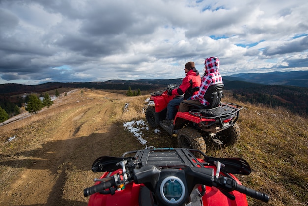 Verbinden Sie das Fahren eines atv in der Front auf die Oberseite des Berges unter Himmel mit Wolken in den Bergen