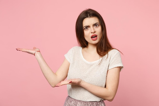 Verblüffte gereizte junge Frau in legerer leichter Kleidung posiert isoliert auf pastellrosa Hintergrund Studioportrait. Menschen aufrichtige Emotionen Lifestyle-Konzept. Mock-up-Kopienbereich. Hände zur Seite zeigen.