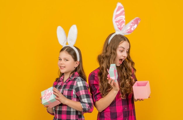 Verblüffte Osterkinder in Hasenohren halten eine Geschenkbox auf gelbem Hintergrund