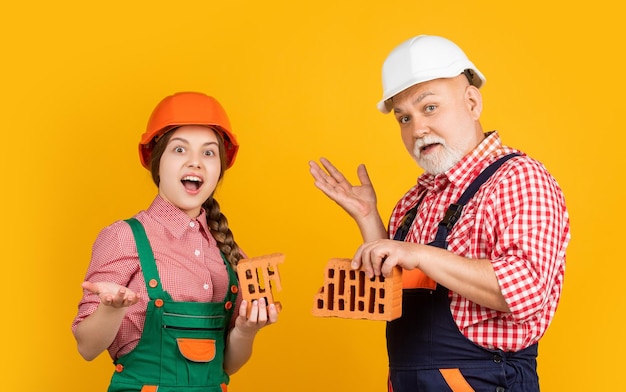 Foto verblüfftes kind und großvater maurer mit helm auf gelbem hintergrund